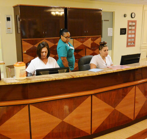 Skilled nurses behind wooden admissions desk at medical facility.