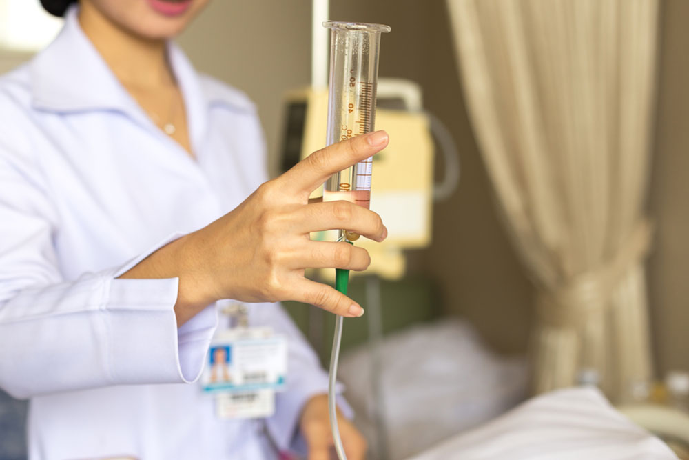 Nurse giving patient water using glass syringe to irrigate nasogastric tube in hospital room